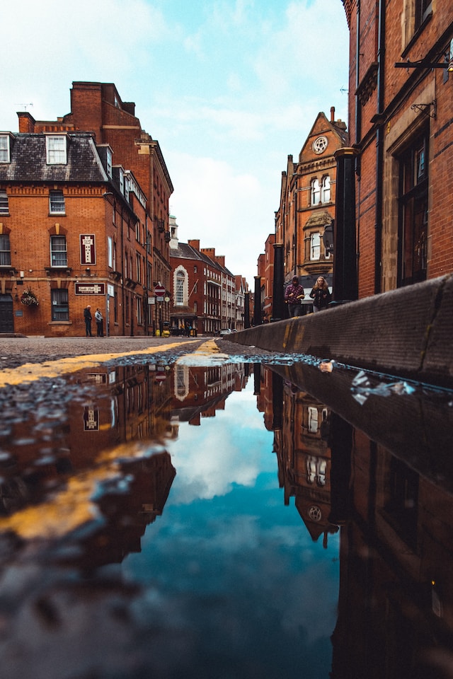 Mirror-like reflection of Leicester's brick buildings on a wet street, showcasing a scenic view perfect for a 'Minibus Hire in Leicester' journey.